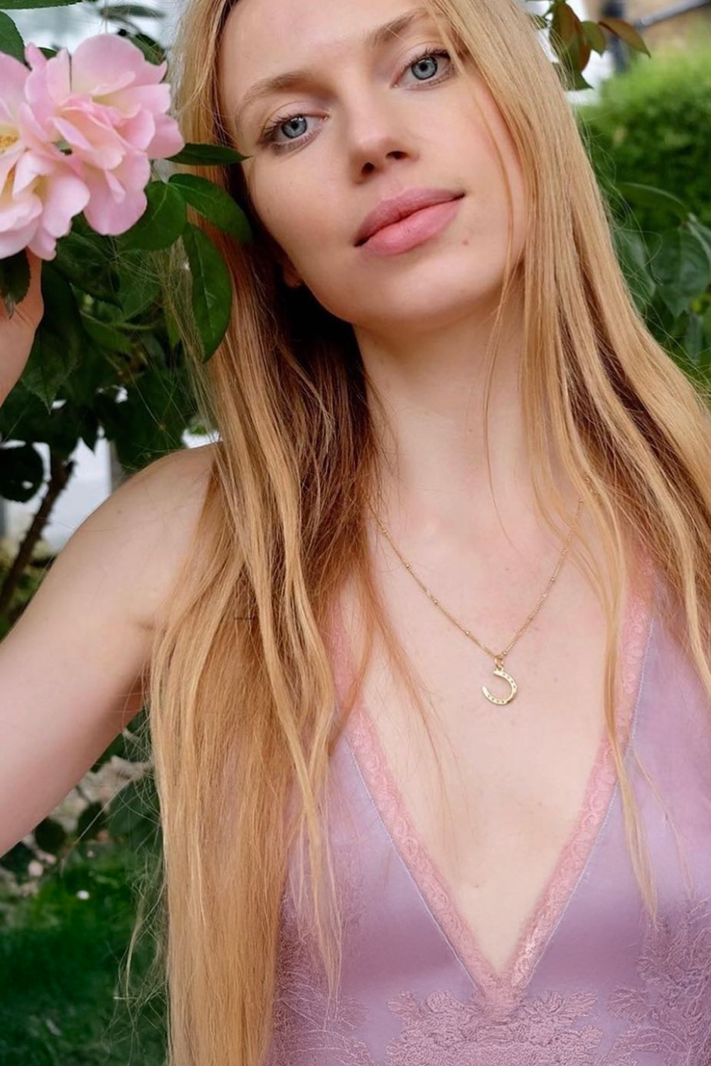 A blond woman model displays a stylish horseshoe necklace, emphasizing personal style and sophistication. A Gold horseshoe necklace for luck. The necklace chain is also gold and has a series of small. Ideal as a unique gift, this pendant celebrates the beauty and strength of horses. Best gifts for horseback riders and one of a kind horse gift ideas for her. A unique horse gift and equestrian