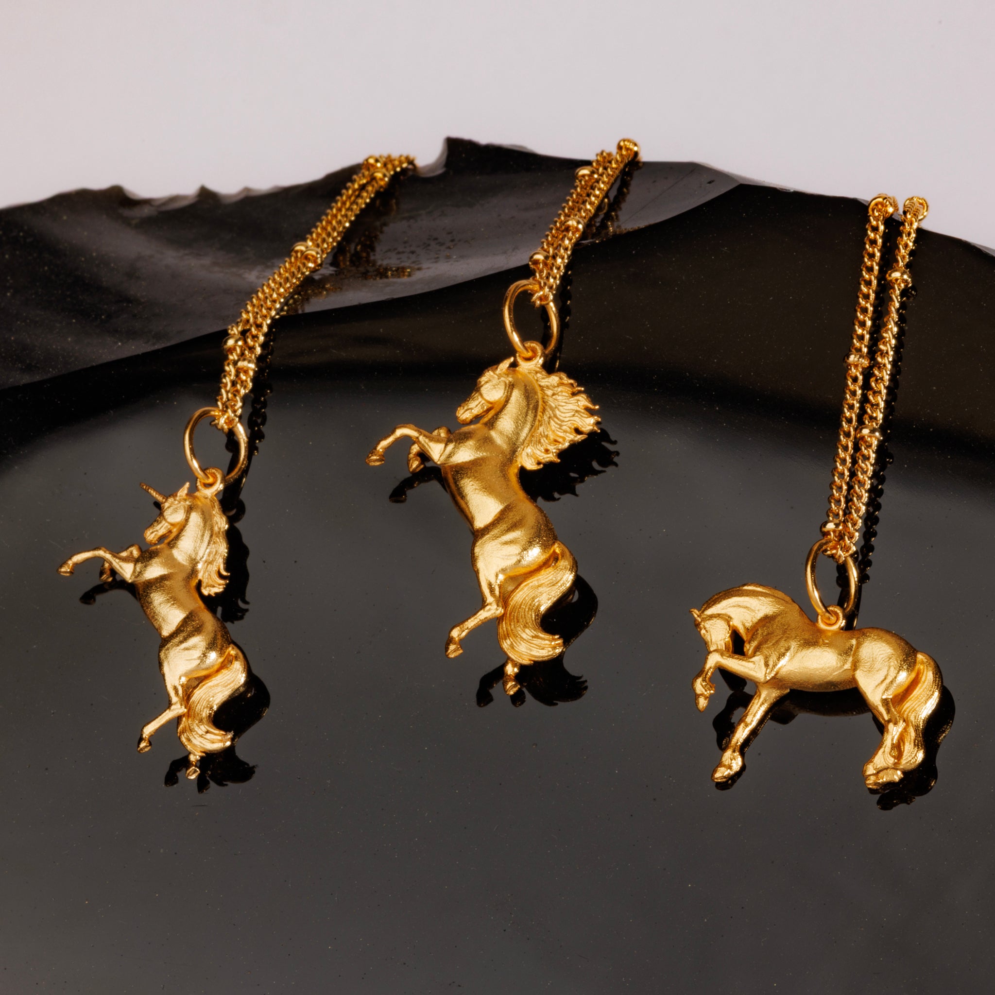 A beautiful image of gold pendant necklaces with rearing and trotting horse designs, perfect for a horse lover.