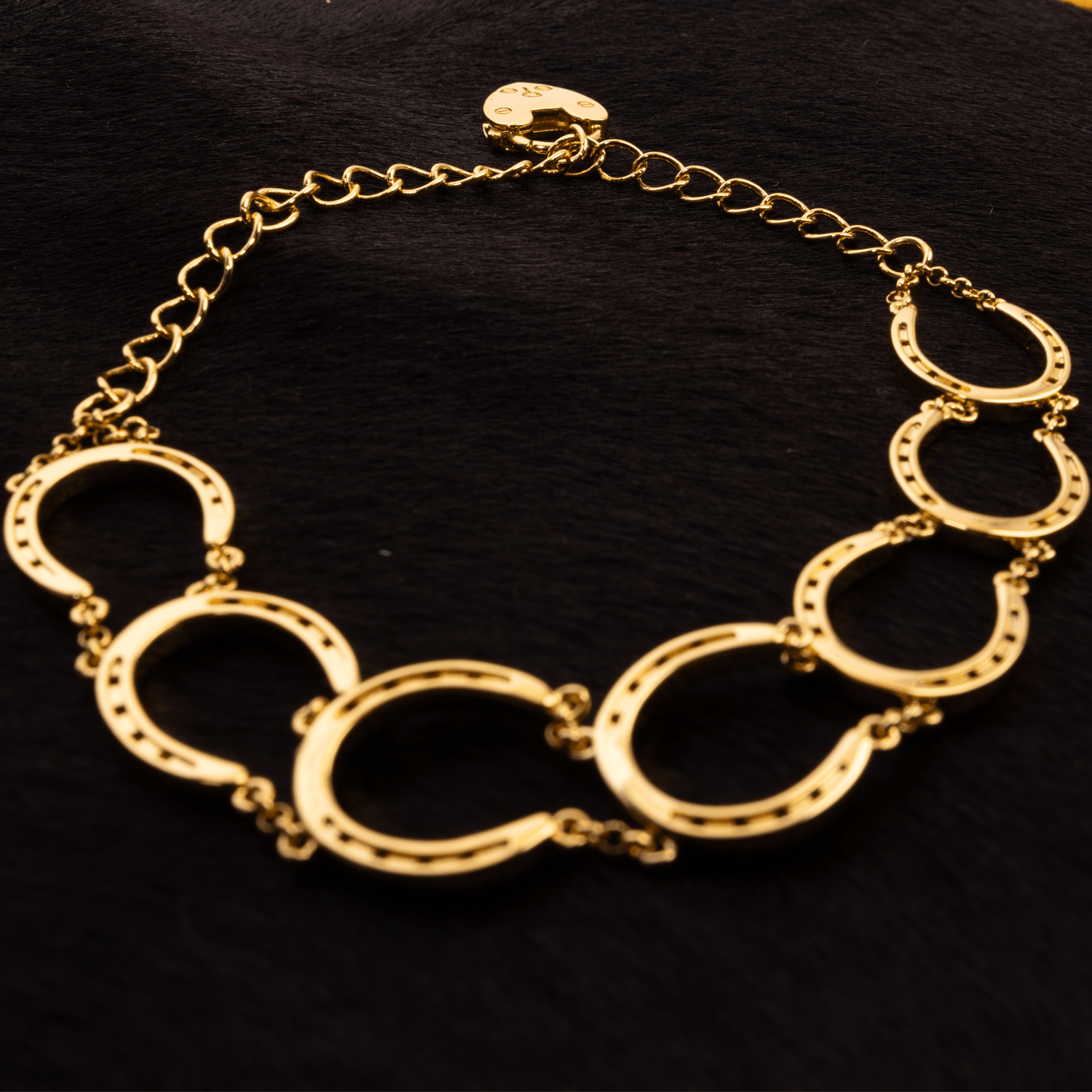 A gold bracelet with seven linked snaffle bit shapes and a heart charm on the chain extender.