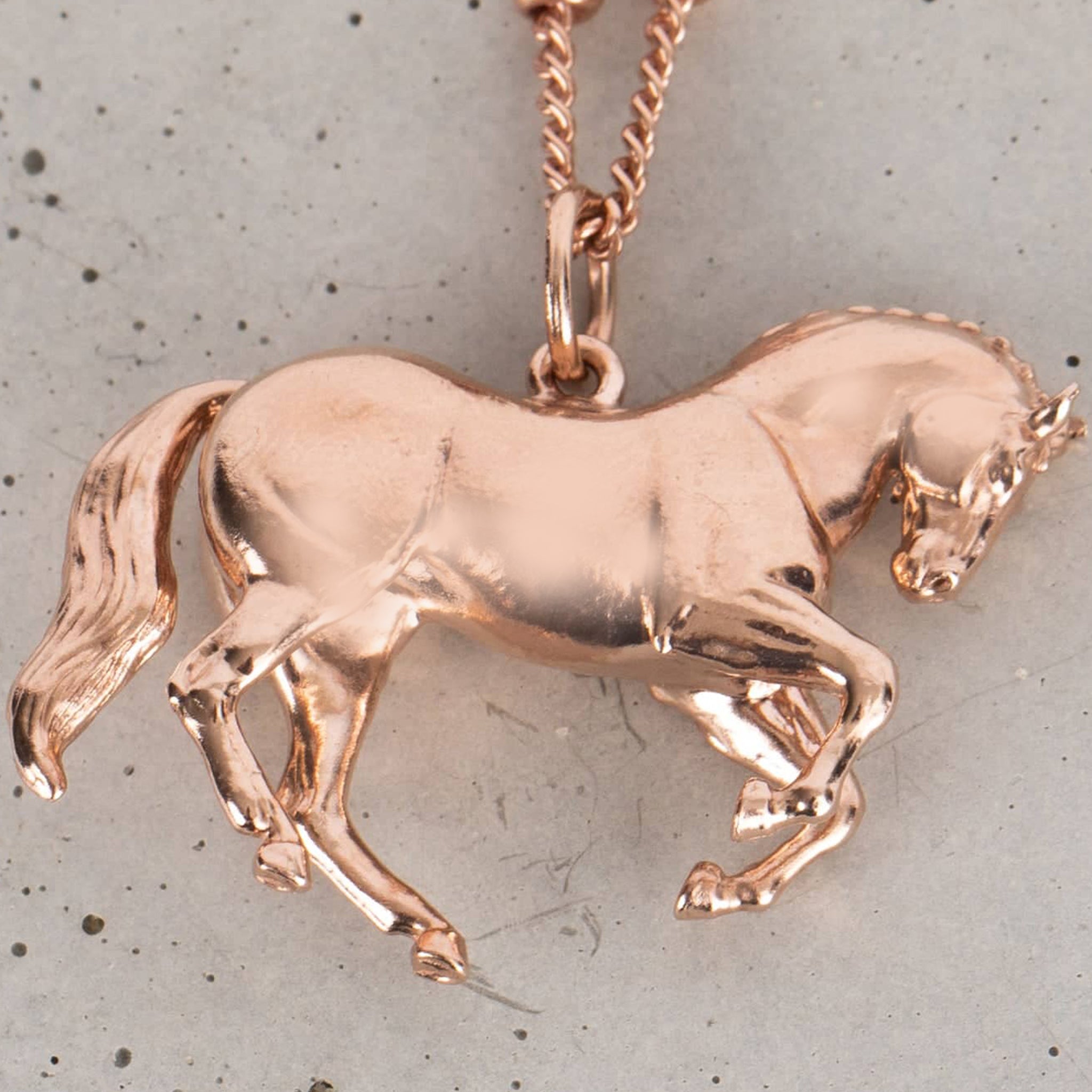 Rose gold horse-shaped pendant necklace on a chain against a gray background
