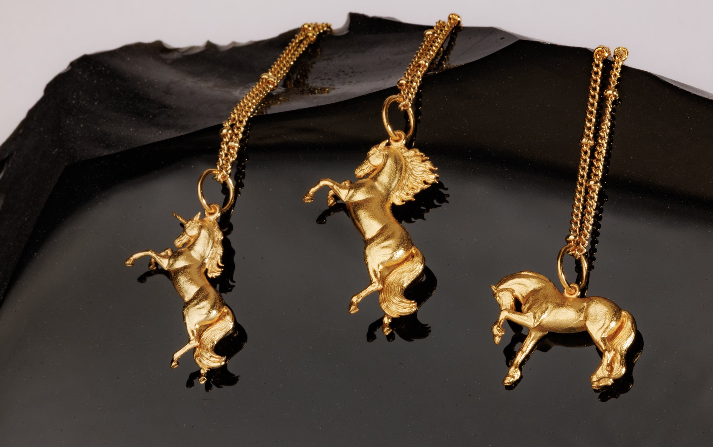 Three elegant gold necklaces featuring distinct horse pendants.