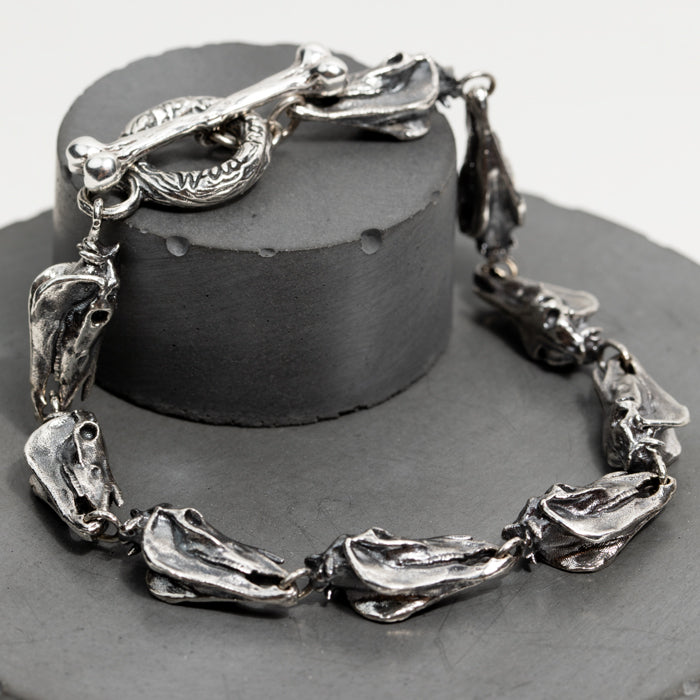 Close-up of a chunky solid silver linked horse skull bracelet with a bone-shaped toggle clasp.