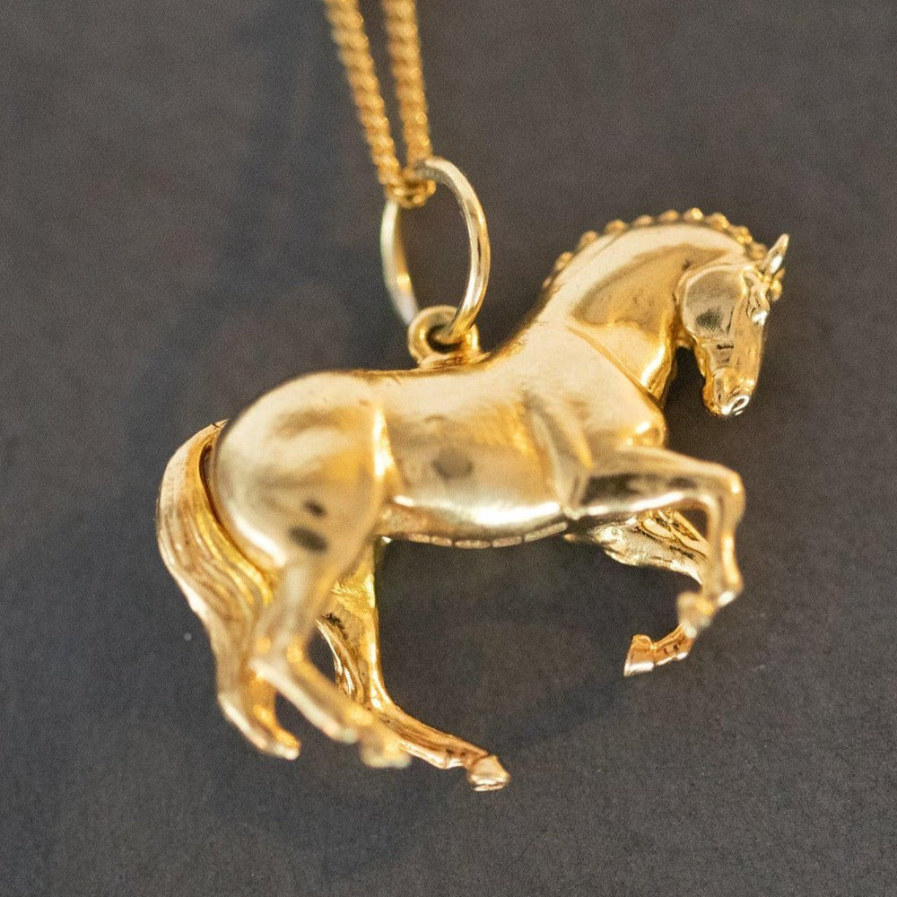 The Perfect Horse Pendant - The Wild Horse Club, a gold horse pendant elegantly displayed, showcasing its intricate design and craftsmanship.The pendant is shaped like a wild horse in mid-stride, with detailed features such as its mane and tail.  The background appears to be a plain or stone , light-colored surface.  Perfect for horse lovers, fans of equestrian inspired jewelry, horseback riders, silver horse jewelry, unique equine gifts, horse girls. A dynamic piece of Horse Jewelry.